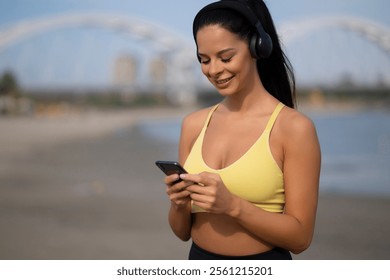 Portrait of young sporty woman using phone to select music for workout - Powered by Shutterstock