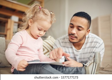 Portrait Of Young Stay At Home Dad Reading Books With Cute Little Daughter While Enjoying Tine Together In Home Interior