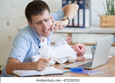 Portrait of young stressed dad trying to work and talk on phone while sitting with his newborn babe in home office interior. Handsome overworked guy making call with his child crying on office table