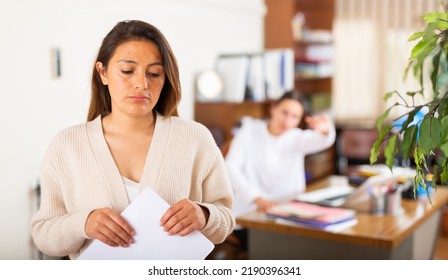 Portrait Of Young Stressed Woman Holding Dismissal Letter At Office