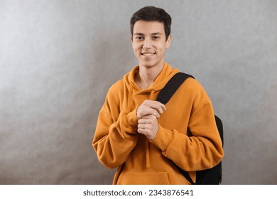 Portrait of a young student with a school bag. The teenager smiles and looks at the camera. A happy teenage boy on a grey background