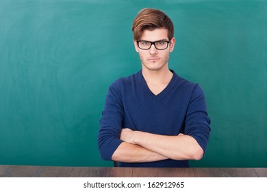 Portrait Of Young Student Standing In Front Of Chalkboard