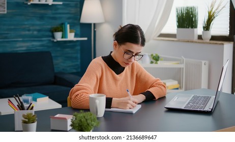 Portrait of young student taking notes on textbook in online class on laptop, attending remote course meeting with teacher. Woman writing university information on notebook to learn. - Powered by Shutterstock