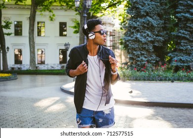 Portrait of young stylish hipster black man in white headphones and sun glasses dancing outdoor in city centre, having some fun - Powered by Shutterstock