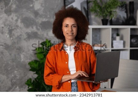 Portrait of young successful African American woman entrepreneur, ffice worker or CEO working using laptop, stands in modern office or coworking