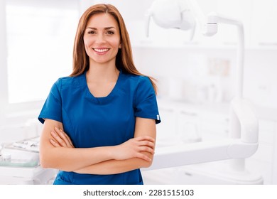 Portrait of young successful confident female doctor wearing uniform standing in ER and smiling with arms crossed