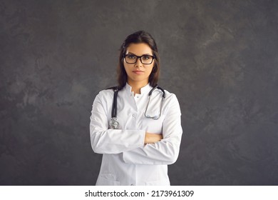 Portrait Of Young Successful Female Doctor Or Nurse In White Medical Uniform Pose On Black Studio Background. Confident Millennial Woman GP Or Therapist In Hospital Wear. Healthcare, Medicine Concept.