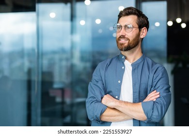 Portrait of a young successful man, businessman, freelancer, designer standing in the office, crossing his arms, confidently looking to the side