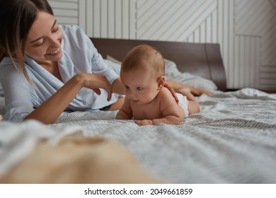 Portrait Of Young Supportive Mother And Cute Naked Baby Both Lying In Bed Enjoying The Moment Together. Tummy Time For Baby With Support Of Loving Mother.