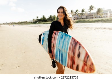Portrait of young surfer woman on the beach holding her surfboard