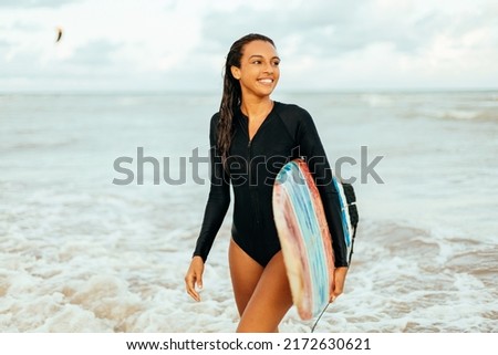 Portrait of young surfer woman on the beach holding her surfboard
