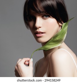 Portrait Of A Young Sweet Girl In The Studio On A Gray Background With A Green Flower In Hand, The Concept Of Beauty And Health