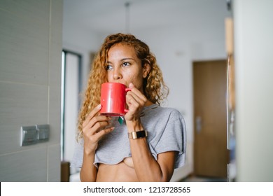 Portrait Of A Young, Tanned And Sexy Indonesian Asian Woman Enjoying A Hot Mug Of Tea On Her Own At Home On A Morning. She Has Dyed Frizzy Hair And Is Wearing Comfortable Home Clothes. 