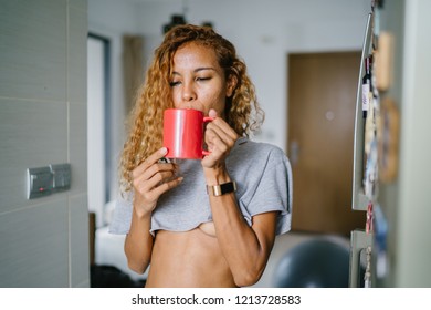 Portrait Of A Young, Tanned And Sexy Indonesian Asian Woman Enjoying A Hot Mug Of Tea On Her Own At Home On A Morning. She Has Dyed Frizzy Hair And Is Wearing Comfortable Home Clothes. 