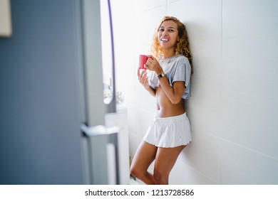 Portrait Of A Young, Tanned And Sexy Indonesian Asian Woman Enjoying A Hot Mug Of Tea On Her Own At Home On A Morning. She Has Dyed Frizzy Hair And Is Wearing Comfortable Home Clothes. 