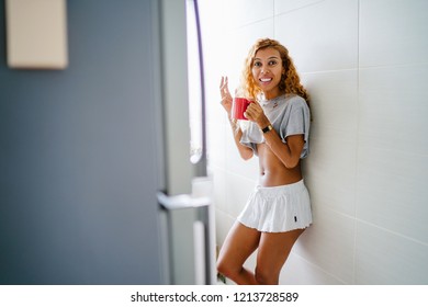 Portrait Of A Young, Tanned And Sexy Indonesian Asian Woman Enjoying A Hot Mug Of Tea On Her Own At Home On A Morning. She Has Dyed Frizzy Hair And Is Wearing Comfortable Home Clothes. 