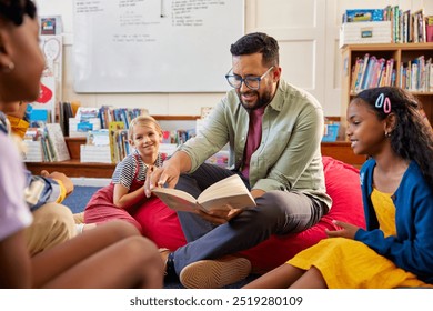 Portrait of young teacher reading book to primary students in school library. Man reading a fairy tale to a group of multiethnic schollboys and schoolgirls. Librarian at primary school reading a story - Powered by Shutterstock