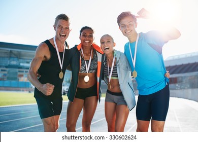 Portrait Of Young Team Of Athletes Enjoying Victory. Diverse Group Of Runners With Medals Celebrating Success.