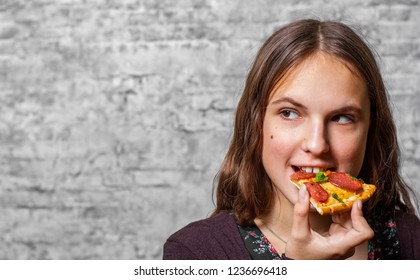 portrait of young teenager brunette girl with long hair eating slice of pizza on gray wall background - Shutterstock ID 1236696418