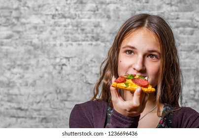 portrait of young teenager brunette girl with long hair eating slice of pizza on gray wall background - Shutterstock ID 1236696436
