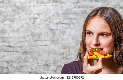 portrait of young teenager brunette girl with long hair eating slice of pizza on gray wall background - Shutterstock ID 1242980692