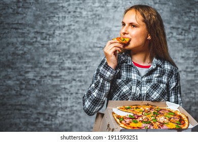 portrait of young teenager brunette girl with long hair eat slice of pizza on gray wall background