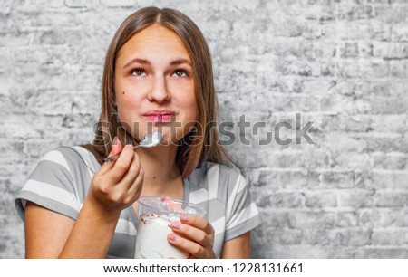 portrait of young teenager brunette girl with long hair eating ice cream on gray wall background