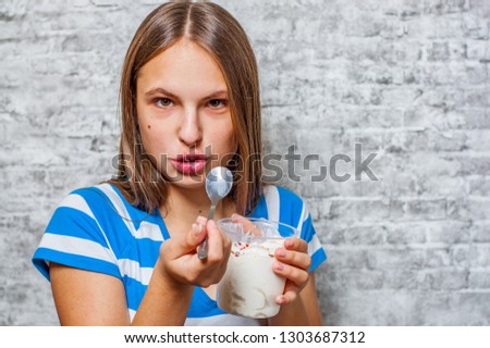 portrait of young teenager brunette girl with long hair eating ice cream on gray wall background