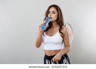 Portrait of a young tennis player hydrating isolated on gray background. - Powered by Shutterstock