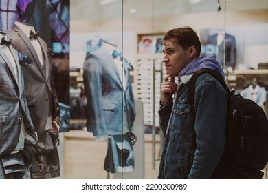 Portrait Of Young Thoughtful Man Considering Showcase In Shopping Center. Concept Of Shopping, Dream, Desire