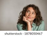 Portrait of young thoughtful woman with hand on chin having an idea against grey background. Pensive woman looking away while thinking. Close up face of girl planning her future isolated on gray wall.
