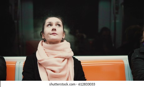 Portrait of young and thoughtful woman sitting in subway. Girl uses public transport, looking around, at window.