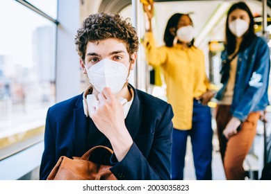 Portrait of young tired handsome caucasian man with medical mask FFP2 KN95 looking at camera sitting in bus with other passengers on blurred background. Train passenger traveling safely in seat. - Powered by Shutterstock