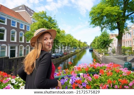Portrait of young tourist woman between flower pots looking at camera on canal in The Hague, Netherlands