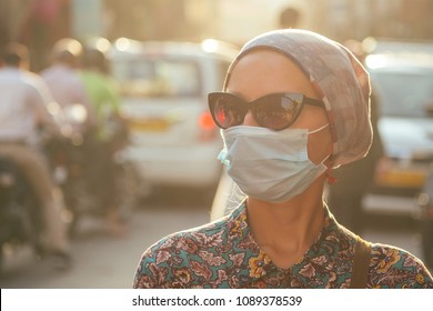 Portrait Of A Young Tourist Woman Wearing Sunglasses And A Mask On The Background Of A Street With Cars And People. The Concept Of Tourism, Health And Safety In The Asian And Indian Countries