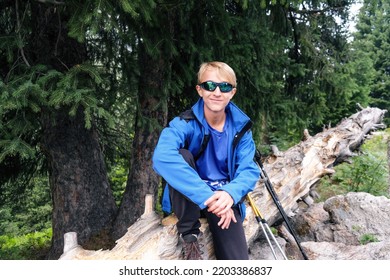 Portrait of a young traveler in a blue jacket and dark glasses sitting on a tree.  - Powered by Shutterstock