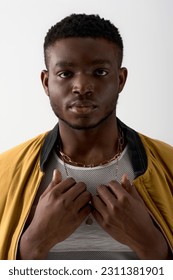 Portrait of young and trendy black model in bomber jacket and golden necklaces looking at camera isolated on grey, contemporary shoot featuring stylish attire, fashion statement