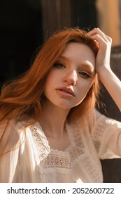 Portrait Of Young White Red Haired Woman Looking At Camera. Judging By Hand Supporting Her Head And Dreamy Expression On Her Beautiful Face, It Seems Like She Is Dreaming About Something Pleasant.