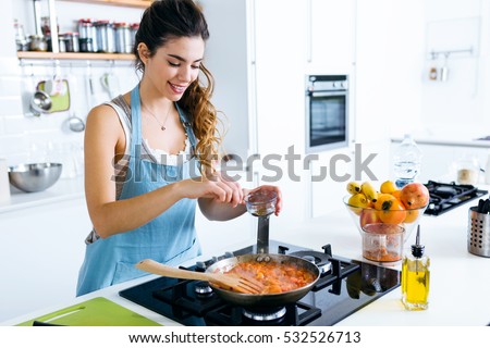 Portrait of young woman adding pepper and mixing food in frying pan.