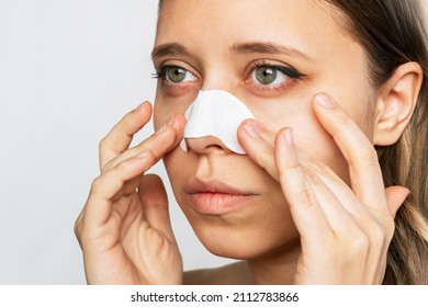 Portrait of a young woman applying nose strips cleaning the skin of her face from blackheads or black dots isolated on a white background. Acne problem, comedones. Enlarged pores. Cosmetology concept