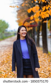 Portrait Of A Young Woman In Autumn. Scenery With Warm Light And Falling Leaves. She Laughs, Authentic Moment.