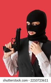 Portrait Of Young Woman In Balaclava With Gun Against Red Background