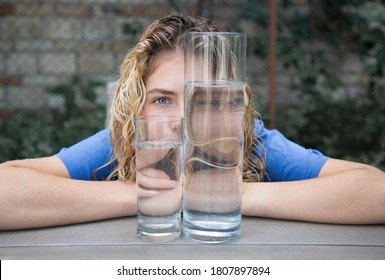 portrait of a young woman with beautiful wavy blond hair through a glass filled with water. Distortion through glass. focus on expressive blue eye. Need to drink water concept