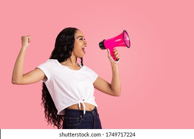 Portrait of a young woman being loud and heard by shouting through megaphone with fist up and mouth open