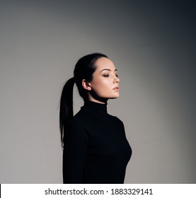 Portrait Of Young Woman In Black Turtleneck With Hairstyle Tail Against Of Grey Background. Side View.