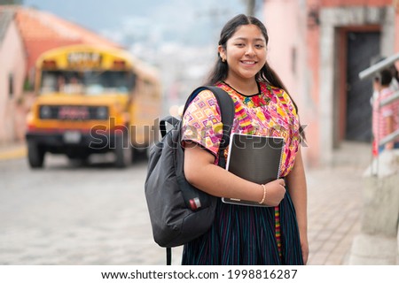 Portrait of a young woman with books and backpack at a bus stop.