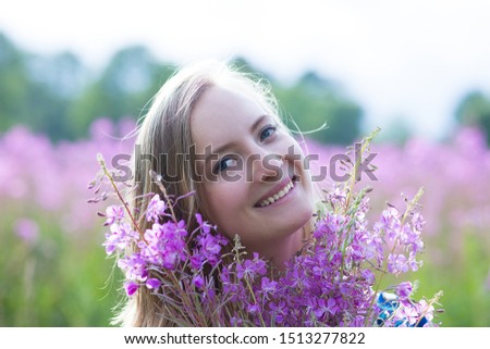Portrait of a young woman with a bouquet of wild flowers. Summer. In the background is a field with pink flowers and green trees.