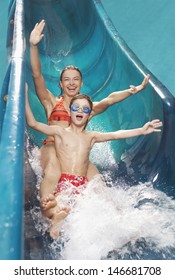 Portrait Of A Young Woman And Boy With Arms Outstretched On Water Slide