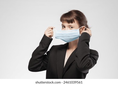 Portrait of a young woman in business attire adjusting a blue medical mask, symbolizing health precautions in professional settings. - Powered by Shutterstock