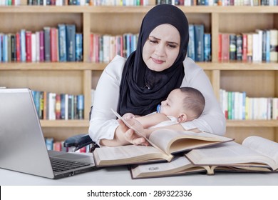 Portrait of young woman carrying baby while reading textbooks in the library